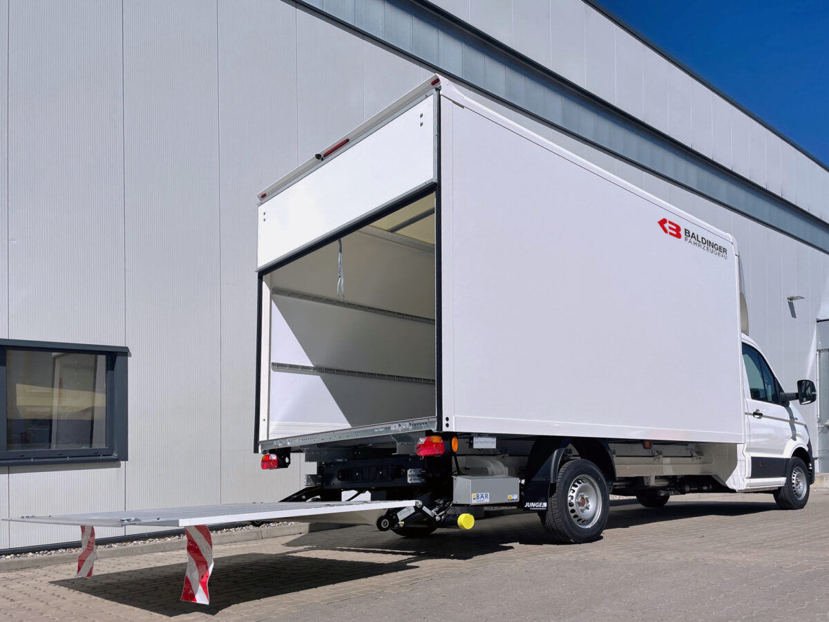 Seitenansicht von hinten: MAN TGE Nutzfahrzeug weiss - Fahrgestell mit Kofferaufbau und easy open Laderampe offen